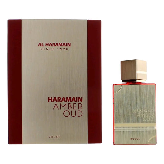 A photo of Al Haramain Amber Oud Rouge 4 oz Eau de Parfum Spray shows a rectangular bottle with a gold cap next to its matching box, both featuring the Al Haramain brand name and logo.